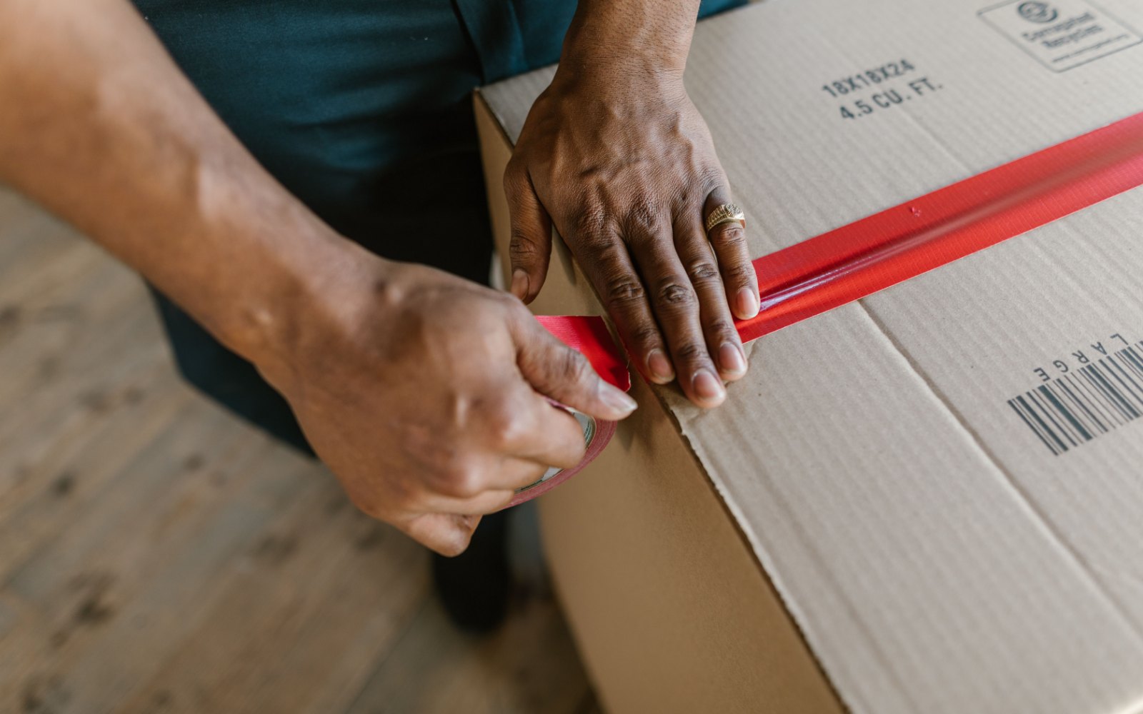 Hands sealing a cardboard moving box with red tape