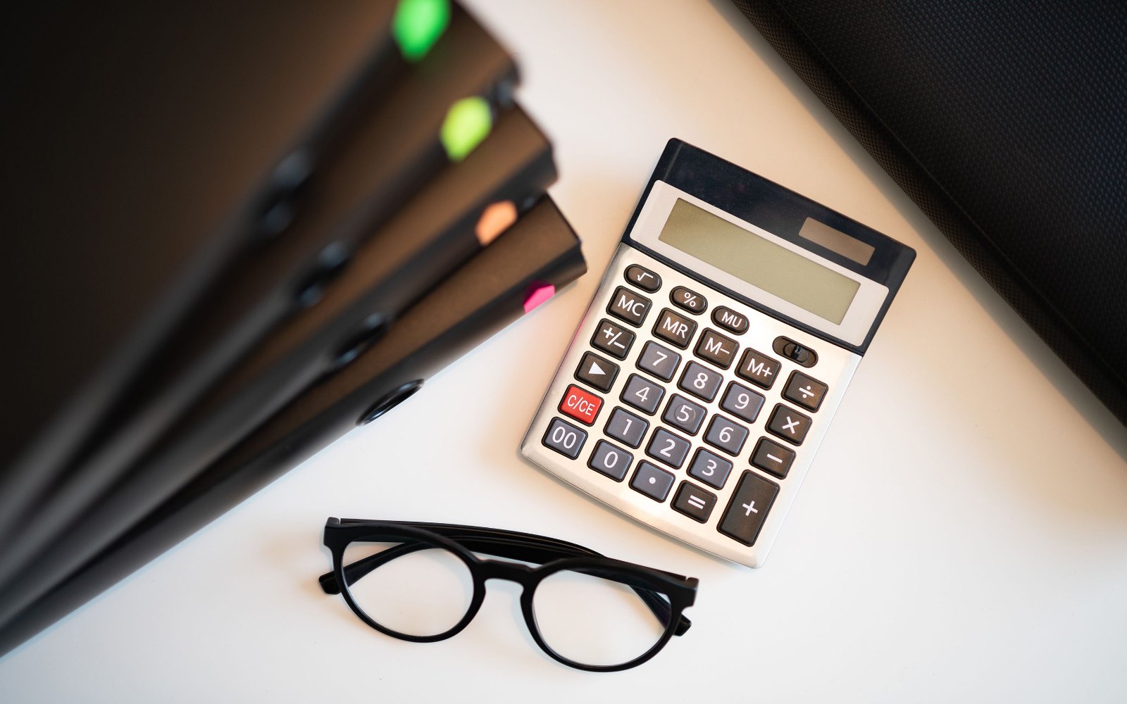 Binders with colourful tabs, a calculator and glasses on a light desk