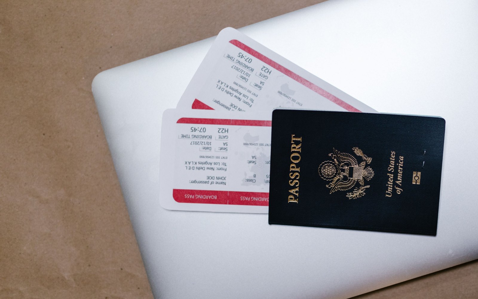 A dark blue United States passport and two boarding passes lying on a closed silver laptop on brown paper